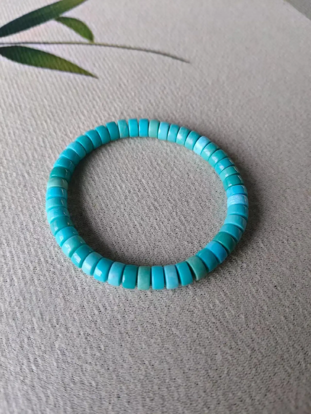 Turquoise-coloured disc bead bracelet on textured fabric.