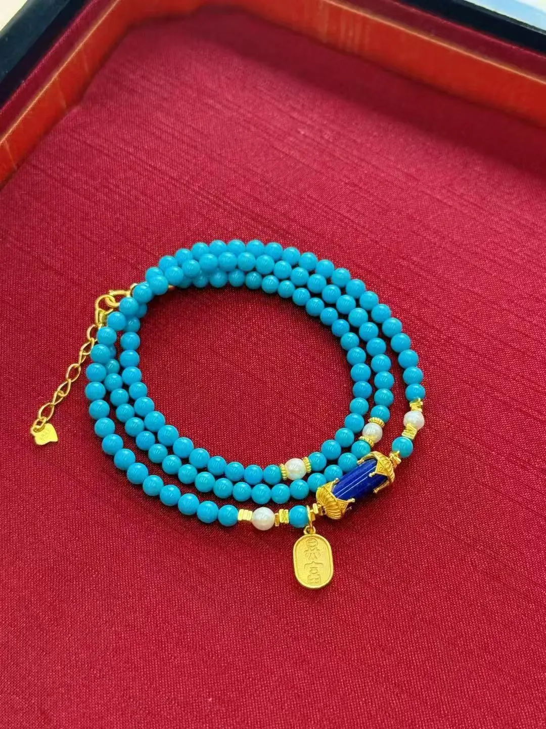 Blue beaded jewellery with gold-tone details on a red tray.